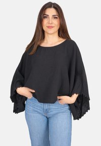 Schwarze Bluse aus strukturiertem Stoff mit weiten Ärmeln und Spitzendetails. Kombiniert mit hellblauen Jeans in lässiger Passform.
