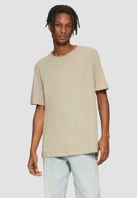 Beige T-shirt met korte mouwen, ronde hals, losse pasvorm, zachte textuur en een effen ontwerp, gecombineerd met lichtblauwe jeans.