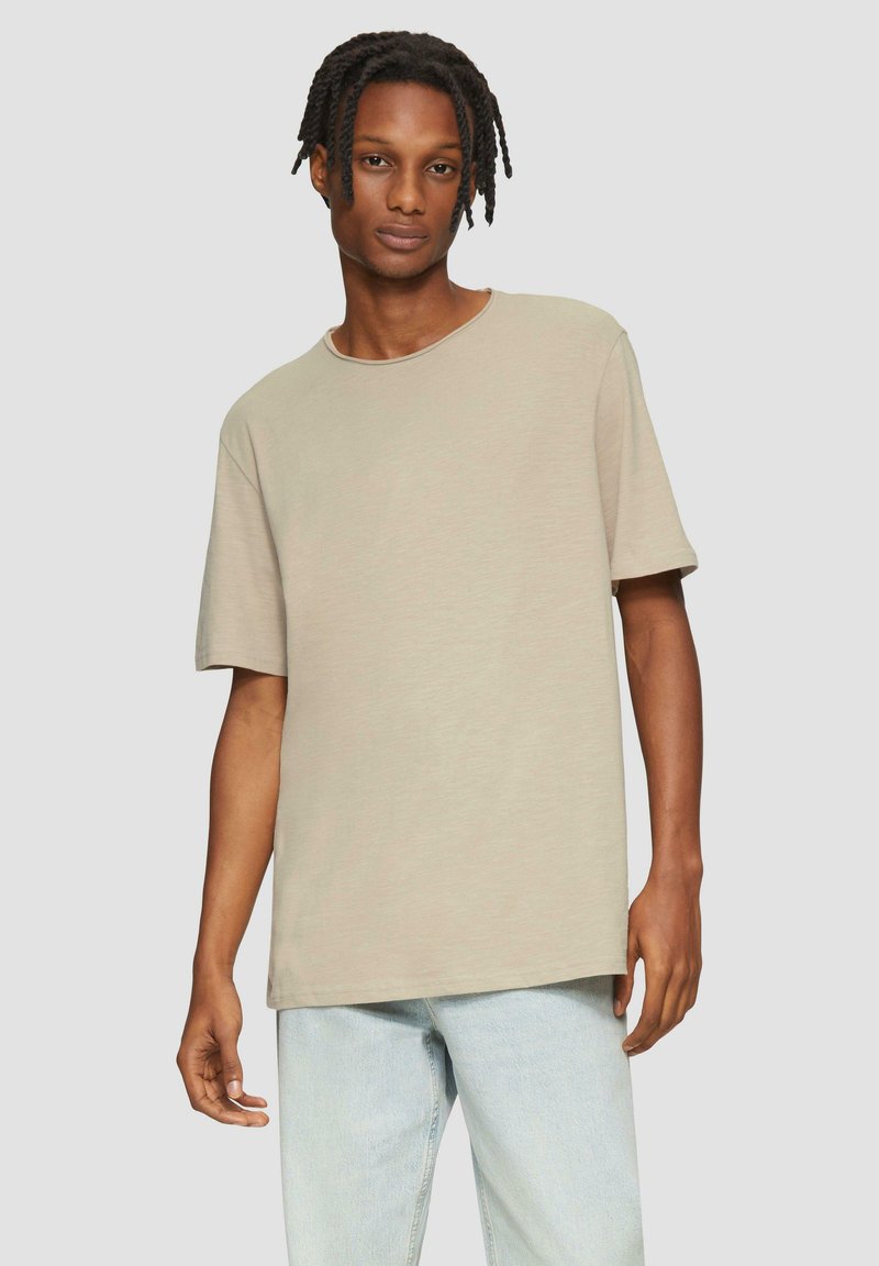 Beige T-shirt met korte mouwen, ronde hals, losse pasvorm, zachte textuur en een effen ontwerp, gecombineerd met lichtblauwe jeans.