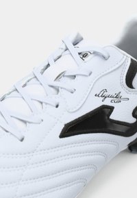 White synthetic football shoe with black accents, featuring textured panels, stitched details, and a lace-up closure. Brand name “eAquila CUP” visible.