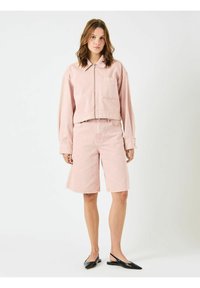 Lyserød denim cropped jakke med en forlommeklap, parret med matchende knælange shorts. Tæt pasform, glat tekstur og minimalistisk design. Sorte flade sko.