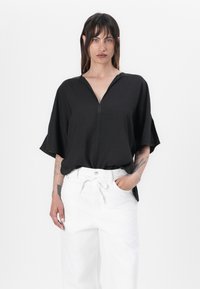 Haut zippé noir à manches courtes, en matériau léger, coupe décontractée. Assorti à un pantalon blanc taille haute au design décontracté.