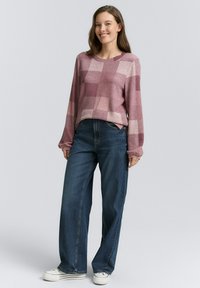 Maglione con un motivo a quadri rosa e mauve, realizzato in tessuto morbido. Abbinato a jeans blu a vita alta e gamba larga e sneakers bianche.