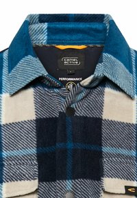 Blauw-wit geruit flanellen overhemd met kraag, voorzien van een knoopsluiting en een contrasterende voering aan de binnenkant, met het label "Camel Active Performance."