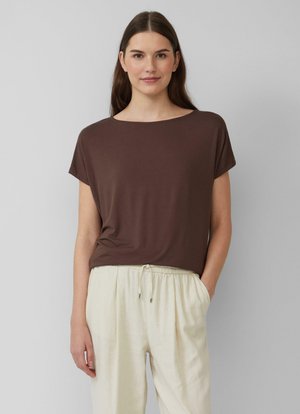 Braunes Kurzarmoberteil, runder Halsausschnitt, weicher Stoff, kombiniert mit hellbeigen Kordelhosen, dezente Textur und lockere Passform.