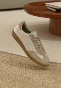 Weiße Sneaker mit beigen Wildlederakzenten, niedrigem Profil, flachen Schnürsenkeln und einer strukturierten braunen Gummisohle.