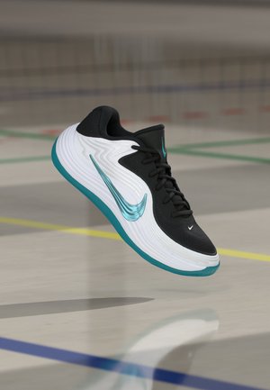 Baskets Nike noir et blanc avec un swoosh turquoise et une semelle flottant au-dessus d'un sol de gym avec des lignes de terrain multicolores.