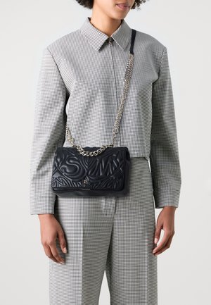Zwarte gewatteerde leren handtas met reliëfontwerp; beschikt over een kettingriem en magnetische sluiting. Gecombineerd met een geruite blouse.