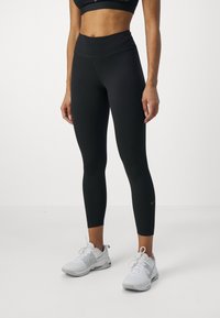 Svarta sportleggings med hög midja, tillverkade av ett slätt tyg. I kombination med grå sportskor med en ljus accent.