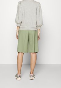 Sudadera gris con mangas abullonadas combinada con pantalones cortos plisados verde claro y zapatillas de colores, tomada desde atrás.