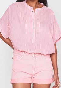 Růžová pruhovaná blůza s krátkým rukávem a kulatým výstřihem, s knoflíkovou légou. Kombinováno s lehce růžovými zkrácenými denimovými šortkami.