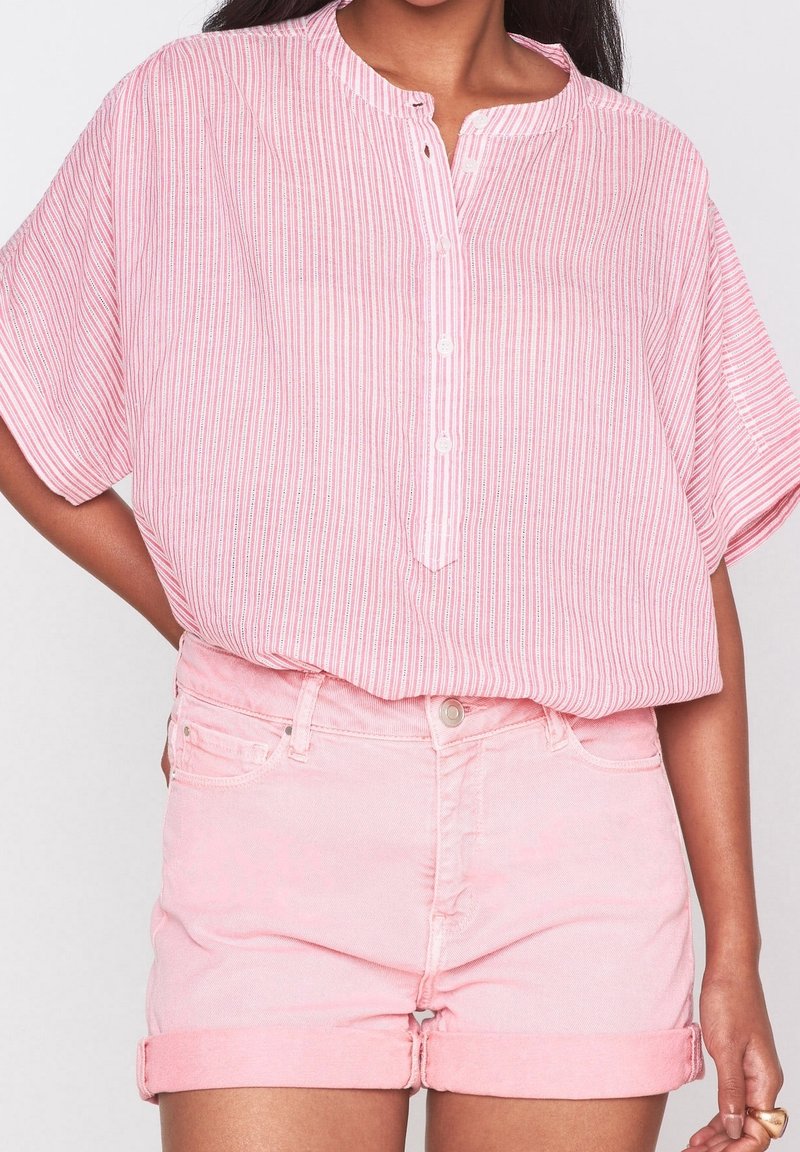 Růžová pruhovaná blůza s krátkým rukávem a kulatým výstřihem, s knoflíkovou légou. Kombinováno s lehce růžovými zkrácenými denimovými šortkami.
