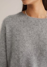 Szary wełniany sweter z okrągłym dekoltem i teksturowaną powierzchnią, o miękkim, puszystym wyglądzie i luźnym kroju.