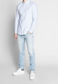 Camicia button-up a righe azzurro chiaro, fit slim, in cotone. Abbinata a jeans azzurro chiaro e sneakers bianche con dettagli blu navy.