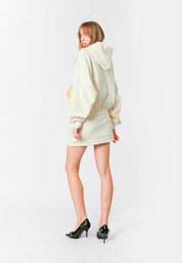 Sudadera con capucha color crema y mangas oversized, combinada con una minifalda a juego. Unos zapatos de tacón negro completan el look.