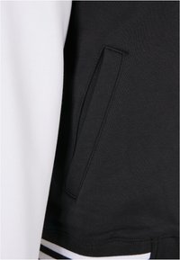 Swarte og kvite sweatshirt med sidelomme, teksturert stoff og stripete kantdetalj. Kontrast i farge mellom ermer og kropp.
