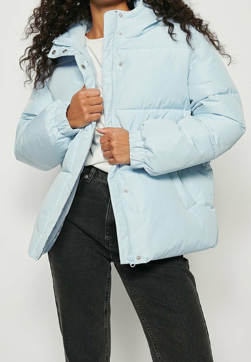 Lyseblå dunjakke med høj krave, trykknapper, elastiske manchetter og sidelommer. Materialet ser glat og isoleret ud.