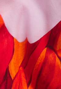 Färggädd tyg med stora röda och orange blommönster på en rosa bakgrund. Texturen verkar mjuk och jämn.