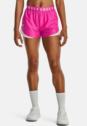 Atletische benen met felroze Under Armour shorts met witte bies, witte sportsokken en witte hardloopschoenen op een effen achtergrond.