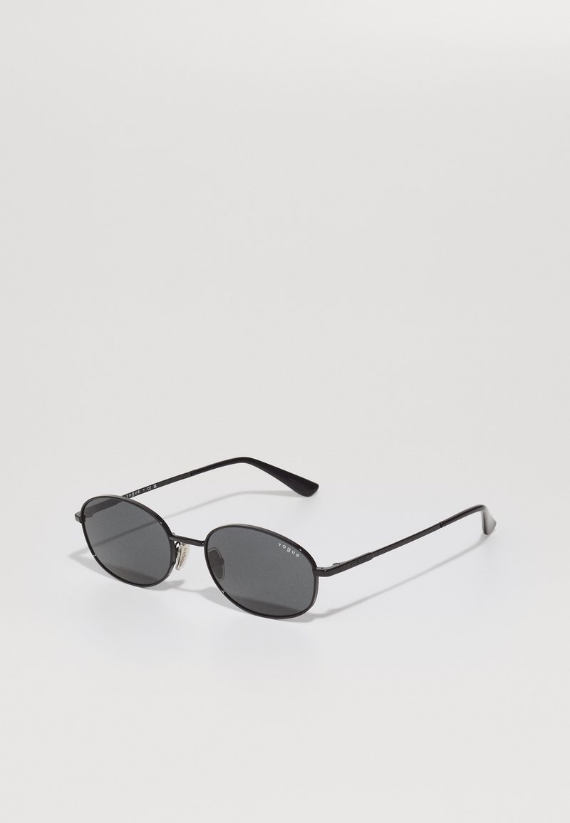 Black oval sunglasses with dark lenses, thin metal frame, and straight temples. Features brand logo on the inner arm and nose pads.