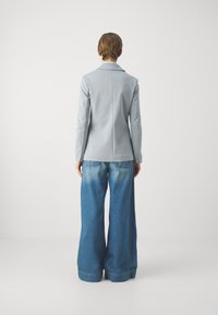 Lichtblauwe blazer met slanke pasvorm over wijde, vervaagde denimbroek. De stof is soepel; de blazer heeft een gelapte kraag en een gestructureerde uitstraling.