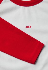 Piros és fehér hosszú ujjú póló kerek nyakkivágással; kontrasztos piros ujjaival, sima tapintásával és egy kis piros "JJXX" logóval a mellrészen.