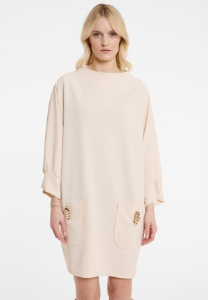 Beiges Kleid mit loser Silhouette, Dreiviertelärmel, zwei vorderen Taschen verziert mit metallischen Akzenten und einem runden Ausschnitt.