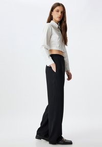 Geknipte witte blouse met lange mouwen, gecombineerd met zwarte broek met elastische taille en zijzakken, gestyled met zwarte flats.