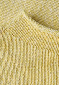 Gros plan sur un tissu tricoté jaune doux avec un motif côtelé et un bord plié.