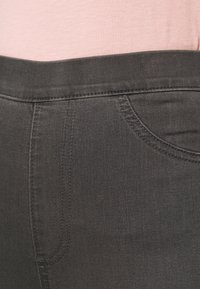 Jean en denim gris foncé avec une texture lisse, présentant un design à cinq poches et des coutures le long des coutures et de la taille.