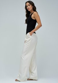 Top negro sin mangas combinado con pantalones anchos y sueltos de color blanco. Textura suave, diseño elegante, bolsillos en la cintura acentuados y detalle de abertura en los laterales.