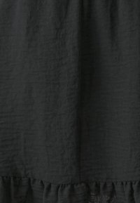 Černá texturovaná tkanina, volánkový lem. Měkký, lehký materiál s mírně zmačkaným vzhledem. Žádné viditelné vzory ani akcenty.