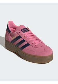 Ροζ σουέτ αθλητικό παπούτσι με μπλε ρίγες, επίπεδα ροζ κορδόνια και υφή σε σόλα από καουτσούκ. Διαθέτει επενδυμένο γιακά και λογότυπο στη γλώσσα.