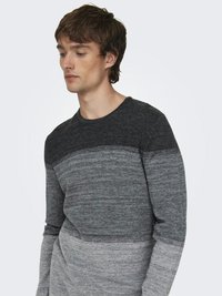 Suéter de punto gris con un patrón de degradado horizontal, con tonos más oscuros en la parte superior y más claros hacia el fondo, escote redondo y mangas largas.