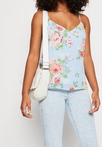 Květinový top s tenkými ramínky v světle modré barvě s růžovými a zelenými růžemi. V kombinaci se světle modrými džíny a tkanou bílou kabelkou přes rameno.