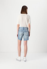 Lettvekts kremfarget mønstret strikket topp og høydejusterte, slitte blå denimshorts. Modellen har på seg hvite høyhælte joggesko.