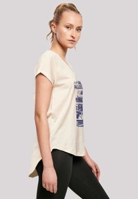 Beige short-sleeve T-shirt made of soft fabric, featuring a blue graphic print on the front. Relaxed fit with a rounded hemline.