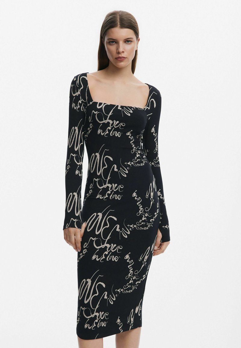 Mustraplekkidega must kleit, millel on pikad varrukad ja ruudukujuline kaelus, ning millel on valge script-muster, mis ütleb "armastus" ja "me armastame".