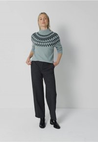 Helles blaues Sweatshirt mit schwarzem Zickzackmuster am Kragen, kombiniert mit dunkelgrauen, weiten Hosen und schwarzen Ankle Boots.