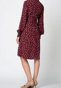 Körsbärröd klänning med vita prickar, långa ärmar, åtsittande midja och medellång fåll, kombinerad med hudfärgade högklackade skor.