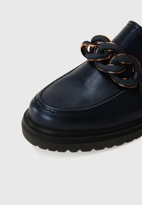 Navy leather shoe featuring a sleek design, prominent chain detail in gold and black, with a chunky black rubber sole.
