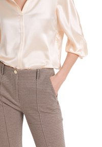 Blouse en satin crème avec un col en V et six boutons, associée à un pantalon marron à motif pied-de-poule. Le pantalon est doté de poches latérales et d'une coupe ajustée.