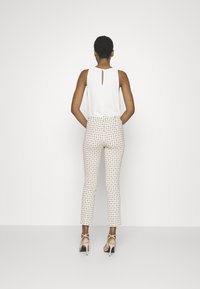 Hvid ærmeløs top med nøglehul detaljer på ryggen, parret med tætsiddende, mønstrede bukser med et geometrisk design i cremede og gyldne nuancer.