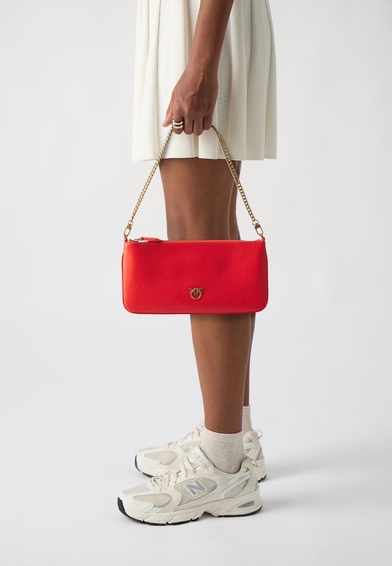 Red leather handbag with a gold chain strap, rectangular shape, zippered closure, and small logo detail on the front.
