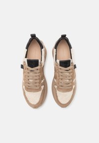 Paire de baskets beige et crème avec un design à lacets, col rembourré noir et semelles épaisses en caoutchouc, vue de dessus sur fond blanc.