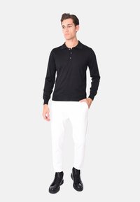 Polo shirt nero a maniche lunghe con colletto a due bottoni, abbinato a pantaloni bianchi e stivaletti neri. Tessuto liscio con polsini a costine.