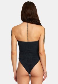 Costume da bagno intero nero con design senza spalline, caratterizzato da un motivo testurizzato e aperture alte sul lato gamba. Dettaglio minimalista sulla schiena.