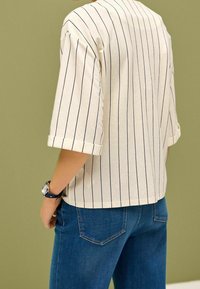 Vaalea raidallinen t-paita, jossa on käännetyt hihat, puuvillakangasta, yhdistettynä sinisiin farkkuihin. Minimalistinen muotoilu, ei näkyviä logoja tai grafiikoita.