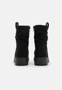 Bottines en daim noir avec un design froncé, des fermetures à glissière sur les côtés, et des semelles en caoutchouc texturé. Équipées de languettes pour un enfilage facile.