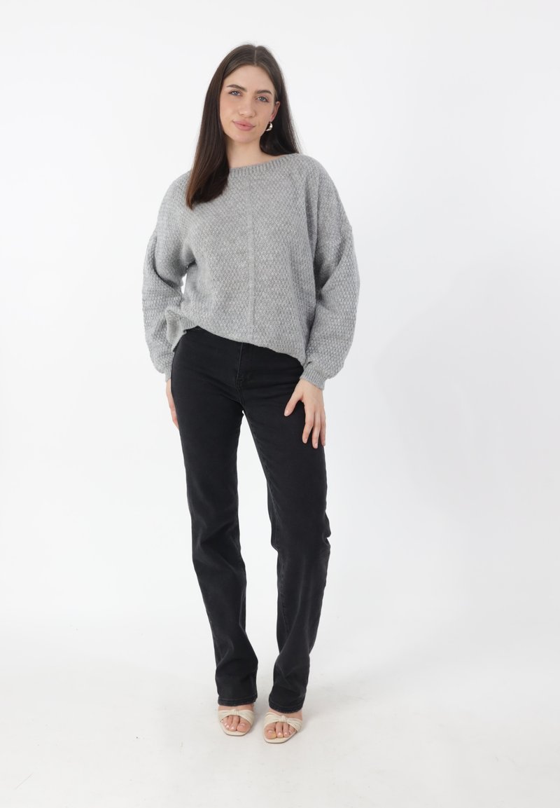 Maglione grigio chiaro lavorato a maglia con vestibilità comoda, maniche larghe e motivo a rilievo, abbinato a jeans neri aderenti e sandali neutri.